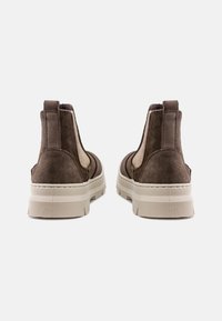 Botas de ante marrón hasta el tobillo con paneles laterales elásticos y una suela gruesa beige, con un acabado texturizado y una lengüeta en la parte posterior.