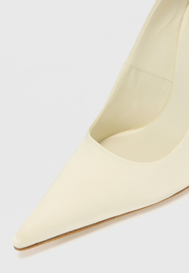 Spitze High Heels aus cremefarbenem Material mit glatter Textur. Verfügt über ein tief ausgeschnittenes Design und einen schlanken Absatz.