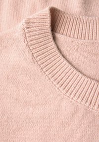 Pull en maille rose pâle doux, léger, avec un col rond côtelé, montrant une texture et des coutures détaillées en gros plan.