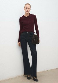Polo de manga larga acanalado en burdeos, jeans de pierna ancha de mezclilla oscura, tacones negros y un bolso redondo de piel de furia marrón. Diseño simple con detalles de botones.