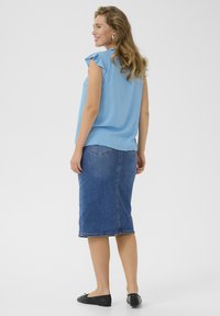 Svetlo modrá blúzka s krátkym rukávom a volánovým detailom, skombinovaná s tmavomodrou džínsovou sukňou po kolená. Celý outfit dopĺňajú čierne balerínky.