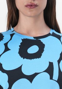 Helles blaues T-Shirt mit großen schwarzen Blumenmustern, einem runden Halsausschnitt und kurzen Ärmeln. Glatte Stofftextur.