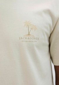 Bež agrumi T-shirt s malim grafičkim prikazom svijetlosmeđeg palminog drveta i natpisom "JACK & JONES OSNOVAN 1990" na lijevoj strani prsnog dijela.