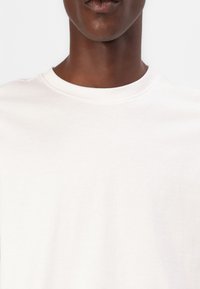 Weißes Baumwoll-T-Shirt mit Rundhalsausschnitt, glatter Textur und minimalistischem Design, das nur den oberen Brustbereich und den Ausschnitt zeigt.