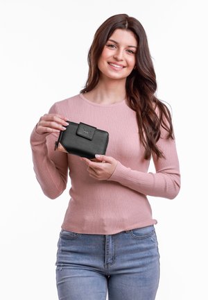 Black leather wallet with a zip closure, rectangular shape, embossed logo on the front, held by a person wearing a pink ribbed sweater.