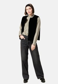 Svart fuskpälsväst över en rutmönstrad skjorta med knappar, ihop med högmidjade mörk denimjeans och svarta loafers. Enkel hårbandaccessoar.