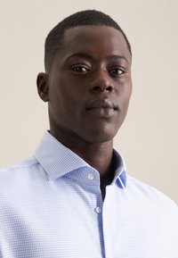 Camicia a quadri blu chiaro con colletto a punta e chiusura con bottoni. Tessuto in cotone, texture liscia e design aderente.