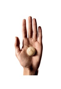 En jevn, rund, blek krem ligger på en åpen menneskehåndflate med lyse hudtoner og veldefinerte fingre mot en hvit bakgrunn.