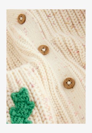 Pletený krémový sveter s textúrovanou tkaninou, ktorý má ružové škvrny, dva drevené gombíky a detail vyšívania zelených listov.