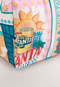 Illustration d'une canette jaune de soda Fanta avec citron, soleil, palmiers, étoiles et texte "FANTA" sur le coin d'un sac en tissu coloré.