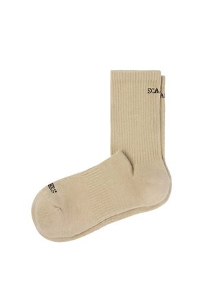 Par de calcetines beige acanalados con logo de texto negro parcial en el puño y la puntera, mostrados planos sobre fondo blanco.
