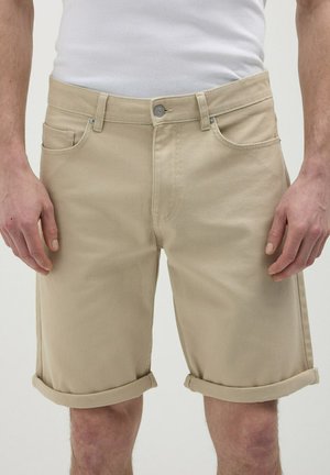 Shorts en denim beige avec des poignets roulés, comportant des poches avant et une fermeture à bouton en métal, texture lisse et coupe ajustée.