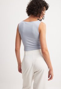 Svetlo modra, oprijeta brezrokavna majica iz rebrastega materiala, v kombinaciji z belimi hlačami visoke pasu. Ima gladko teksturo in preprost dizajn.