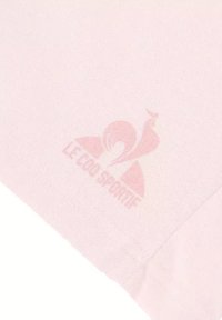 Un tissu rose clair avec une texture lisse présente le logo "Le Coq Sportif" dans une teinte rose plus foncée, sur un fond doux.