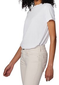 T-shirt blanc à manches courtes avec un col rond, associé à un jean beige clair ajusté. Le tissu semble lisse et léger.