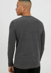 Graues Langarmshirt aus einem weichen Stoff; mit Rundhalsausschnitt, leichter Textur und kontrastierenden Nähten am Saum.