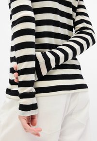 Top de rayas blancas y negras de manga larga con puños ajustados. Material de mezcla de algodón, ajuste relajado, costuras visibles, combinado con pantalones blancos.