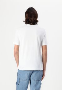 Hvid bomulds t-shirt med korte ærmer, standard rund hals og ensfarvet rygdesign. Bæres med lyseblå cargobukser med lommer.