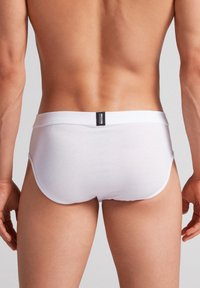 Weiße Baumwollslips mit einem schmalen Bund und einem kleinen schwarzen Etikett. Der Stoff wirkt glatt und enganliegend und betont die Konturen des Körpers.