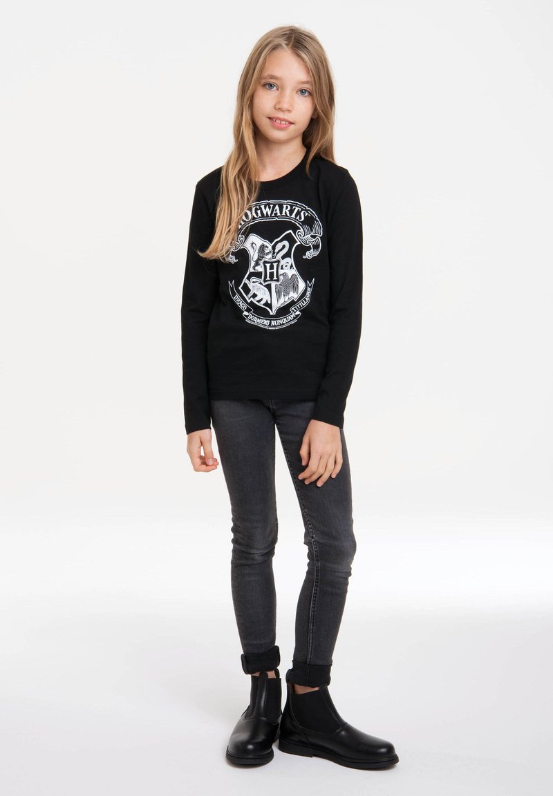 Schwarzes Langarmshirt mit dem Hogwarts-Wappen, kombiniert mit dunkelgrauen Jeans und schwarzen Stiefeletten. Schlichtes Design mit glatter Textur.