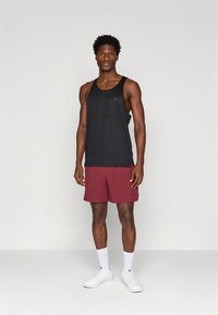 Svart linne och vinröda shorts, båda i syntetmaterial. Linnet har rund halsringning; shortsen är knäförsedda med en lätt glans och logotypdetalj.