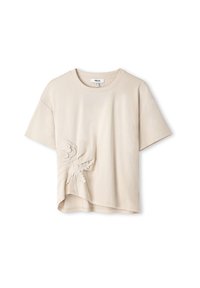 Beżowa koszulka z krótkim rękawem o zaokrąglonym hemie, z teksturowaną haftowaną florą po lewej stronie. Wykonana z miękkiej bawełny.