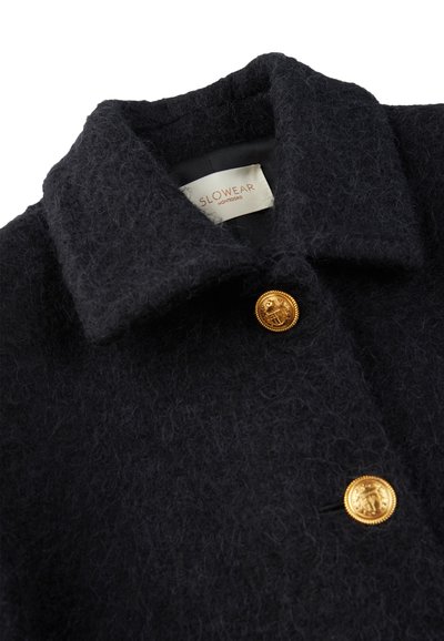 Abrigo de lana en un azul marino oscuro con un acabado suave y texturizado. Presenta un cuello ancho y un botón dorado con un diseño en relieve. Etiquetado en el interior.