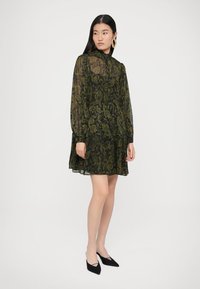 Črna obleka z olivno zelenim vzorcem paisley, z visokim izrezom in dolgimi rokavi, z večplastno krilom in prozorno teksturo.