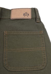 Green fabric pants with a brown leather back patch featuring "BR" logo. Includes a single back pocket with visible orange stitching.