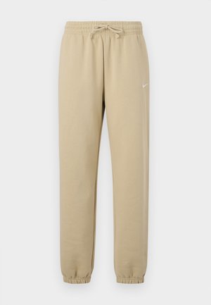 Pantalon de survêtement en coton beige avec ceinture élastique et cordon de serrage, doté de poignets côtelés et d'un petit logo blanc sur le côté gauche.
