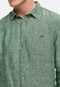 Camicia verde in lino con bottoni in legno, colletto a punta e piccolo logo ricamato blu sul petto.