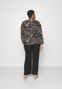 Top negro y beige con estampado y mangas largas, combinado con pantalones negros con plisados y zapatos de tacón cuadrado beige.