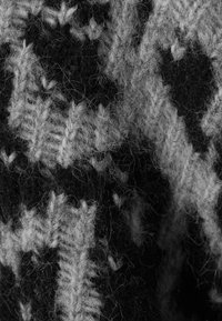 Tissu en laine tricoté présentant un motif géométrique en noir et gris. La texture est douce avec des fibres visibles et une apparence chaleureuse.