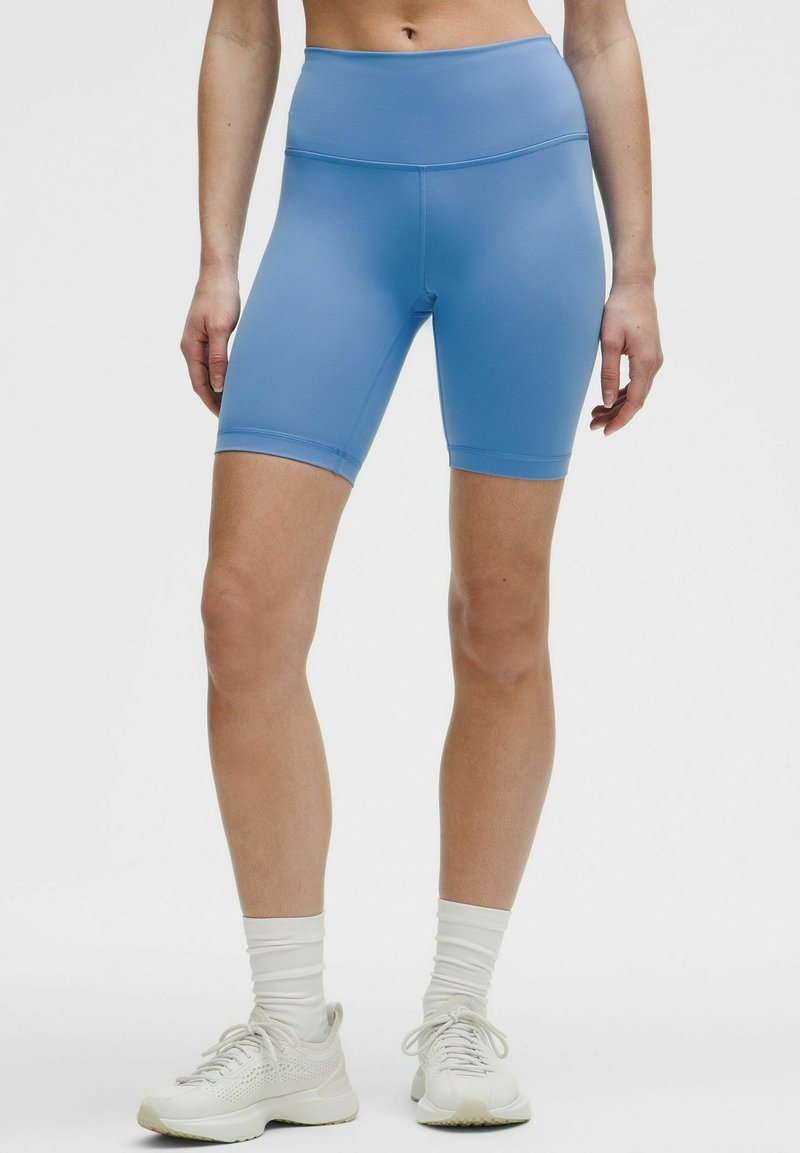 Ljusblå cykelbyxor i stretchmaterial med hög midja, slät yta och knälång design. Kombineras med vita sneakers.