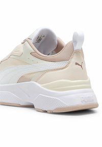 Chaussure de sport avec un mélange de matériaux beige et blanc, dotée d'une tige en mesh texturé, d'un col rembourré et d'une semelle en caoutchouc blanche audacieuse.