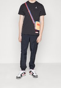 Svartfärgad t-shirt med pinstripe, prydd med en liten logotyp, tillsammans med mörka cargobyxor. Outfiten kompletteras med vita och röda sneakers samt en färgglad crossbody-väska.