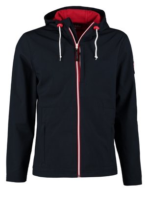 Mann trägt schwarze Jacke über weißem T-Shirt, schwarze Hose, bordeauxrote High-Top-Sneaker, trägt einen Camouflage-Rucksack über einer Schulter.