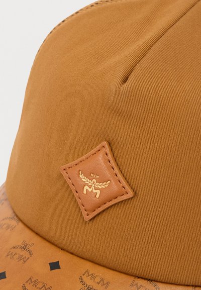 Καφέ καπέλο με υφασμάτινη υφή και δερμάτινο έμβλημα με χρυσό λογότυπο. Το γείσο έχει σχέδιο με μικρές μαύρες λεπτομέρειες.