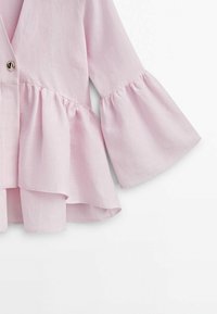 Haut à manches cloche rose en tissu léger avec un design superposé, présentant un bouton central et des accents de drapés doux.