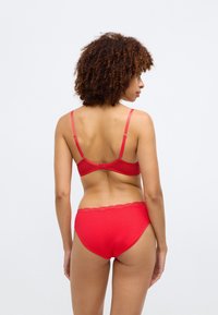 Soutien-gorge rouge et culotte assortie en tissu lisse. Le soutien-gorge a des bretelles réglables et une fermeture à crochet, la culotte présente une bordure en dentelle le long de la taille.
