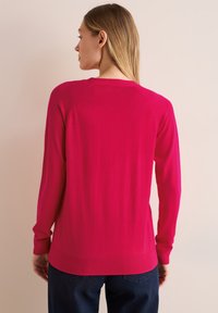 Pull en tricot fuchsia à manches longues, avec des poignets et un ourlet côtelés. Il présente un col rond et une texture lisse. Vue arrière présentée.