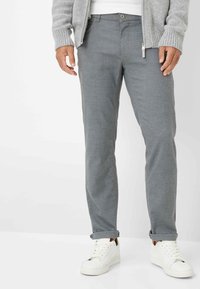 Graue, strukturierte Hosen mit Slim-Fit, ausgestattet mit Fronttaschen und einem Reißverschluss. Kombiniert mit weißen Turnschuhen, die mit umgeschlagenen Säumen versehen sind.