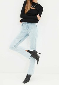 Top negro de manga larga combinado con jeans de tiro alto de color azul claro con aberturas laterales, usados con botas de tacón puntiagudas negras.