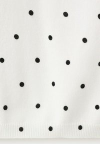 Tissu blanc avec de petits pois noirs uniformément espacés et un ourlet côtelé en bas.