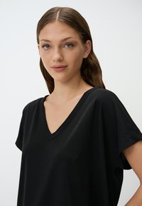 T-shirt nera a V con maniche corte, realizzata in tessuto liscio e dalla vestibilità comoda. Presenta un design semplice e pulito, senza motivi o dettagli.