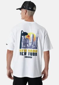 T-shirt bianca a maniche corte con una grafica dello skyline di New York in viola e giallo, con un sole e un pallone da basket. Materiale in cotone, vestibilità comoda.