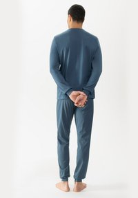 Blauwe langemouwen top met ronde hals, gecombineerd met blauwe gestreepte pyjamabroek; zachte stof, relaxte pasvorm en elastische manchetten bij de enkels.