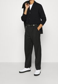 Svart knäpptermokardigan, vit t-shirt under, skräddarsydda svarta byxor och vita skor med tjock svart sula. Silverfärgad bälteskedja som detalj.