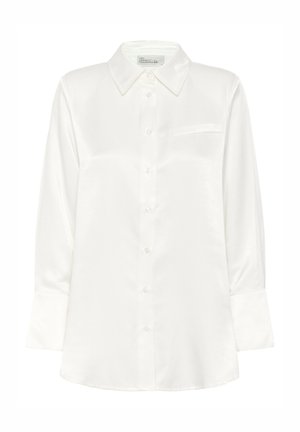 Chemise blanche à manches longues en satin, boutonnée avec un col pointu et une poche poitrine passepoilée, étiquetée "Mon Garde-Robe Essentielle."