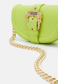 Borsa a tracolla in pelle verde con hardware dorato, caratterizzata da una tracolla a catena e una chiusura decorativa. Forma arrotondata con dettagli cuciti.